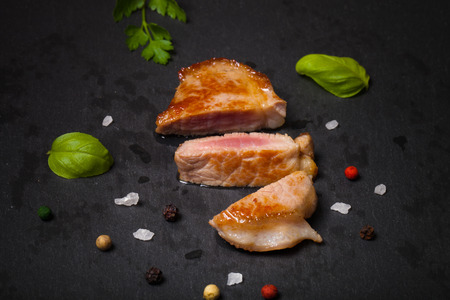 Fried meat with herbs and spices on a black slate plate. Selective focus. Toned.の写真素材