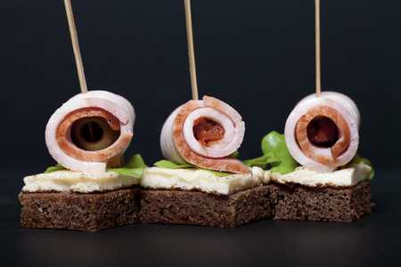 Small snacks canape with brisket, rye bread, omelet and lettuce on skewer on a black slate plate. Selective focus. Toned.の写真素材