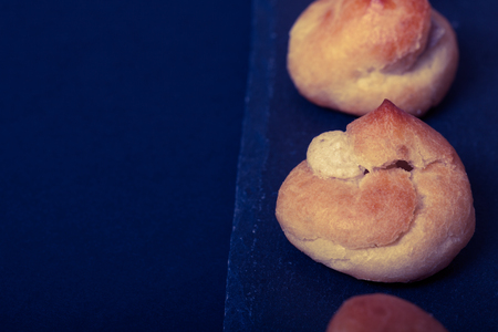 Set of small profiteroles on a black slate plate. Selective focus. Toned.