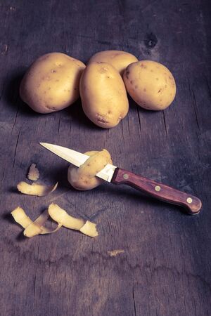 Potatoes with peelings on old wooden background. Toned.の写真素材