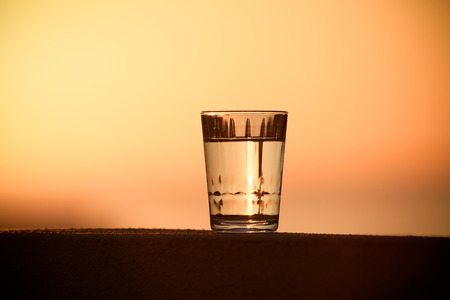 Glass of water on the background of beautiful sunset. Selective focus. Toned.