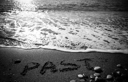 Wave and inscription "PAST" on the pebble coast of sea. Selective focus. Toned.の写真素材