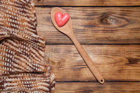 Knitted scarf, wooden spoon and red hearts on old wooden burned table or board for background.