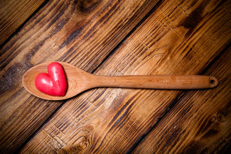 Wooden spoon and red hearts on old wooden burned table or board for background. Toned.の写真素材