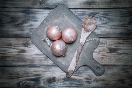 Fresh onion and retro cutting board on old wooden burned table or board for background. Toned.