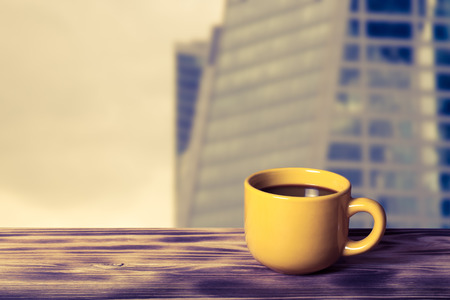 Coffee in cup on wooden table opposite a defocused cityscape for background. Collage. Selective focus. Toned.の写真素材