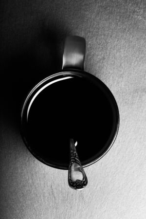 Mug of black tea with melchior spoon on black slate table. Top view. Toned.の写真素材