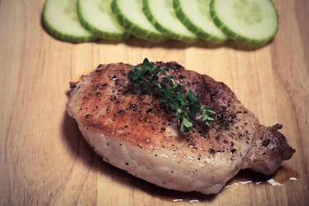 Fresh fried meat with thyme, garlic and cucumber on light wooden cutting board. Selective focus. Toned.の写真素材
