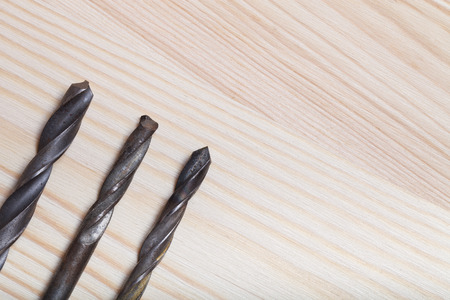 Old drills on light wooden background. Top view.