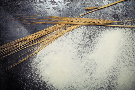 Wheat ears and sprinkle flour on black background. Toned.の写真素材