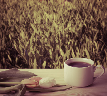 Tea cup with tulips on the wooden table opposite blurred background. Collage. Selective Focus. Toned.の写真素材