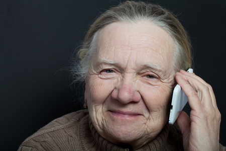 Portrait of elderly woman with telephone on dark background.の写真素材