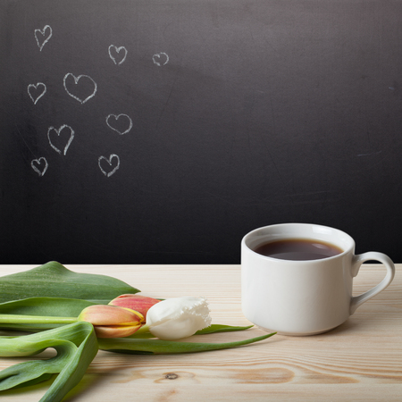 Romantic theme on a chalkboard behind a wooden table with cup of coffee and tulips.の写真素材