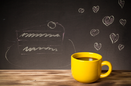 Romantic theme on a chalkboard behind a wooden table with cup of coffee. Toned.の写真素材