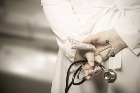 The doctor put his hands with stethoscope and money behind his back on a blurred background. Toned.の写真素材