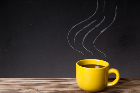Steam pattern on a chalkboard behind a wooden table with cup of coffee.の写真素材