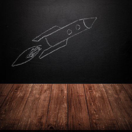 Children's drawing a rocket on a chalkboard behind a wooden table. Toned.の写真素材