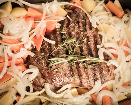 Large piece of fresh beef meat prepared on a grill pan with herbs and vegetables. Toned.の写真素材