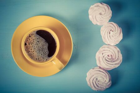 Fresh pink homemade zephyr - marshmallow and cup of coffee on blue wooden table. Toned.の写真素材