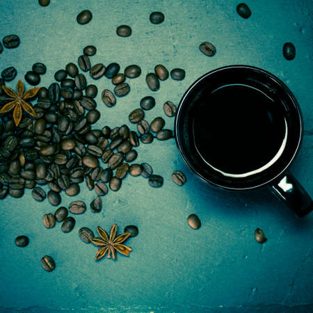 Black cup of coffee and coffee seeds on the slate background. Toned.