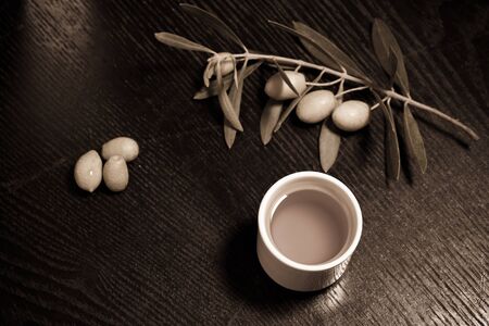 Branch of olive tree with green olive berries and cap of fresh olive oil on a black wooden table or board. Toned.の写真素材