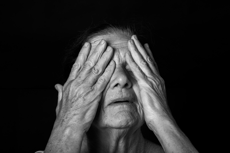 Portrait of elderly woman. Closes eyes with hands. Toned.の写真素材