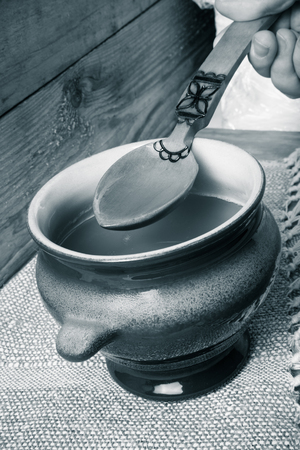 Clay pot with ghee and spoon on linen napkin. Rustic still life. Wooden background. Toned.の写真素材