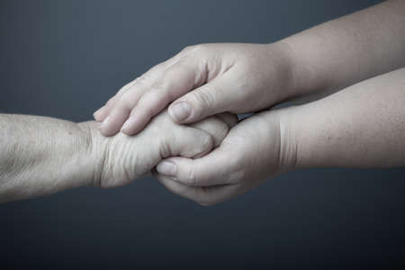 Hands of elderly and young women on black background. Toned.