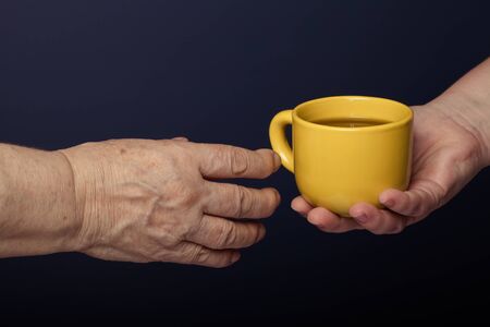 Hands of elderly and young women on black background. Toned.