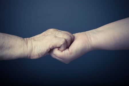 Hands of elderly and young women on black background. Toned.の写真素材