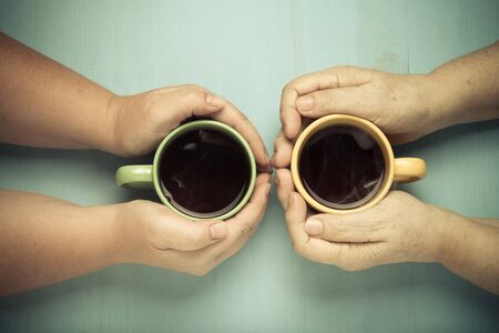 Hands of elderly and young women on wooden background. Toned.
