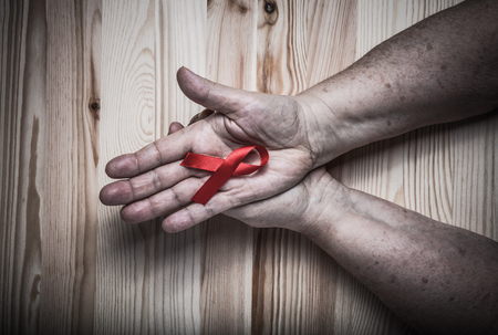 Hands of elderly woman and an international symbol of the fight against breast cancer on light wooden background. Toned.の写真素材