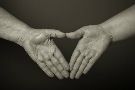 Hands of elderly and young women on black background. Toned.の写真素材