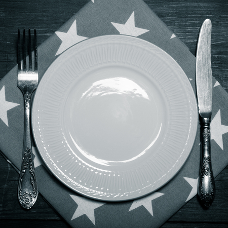 Plate, fork and knife on napkin on wooden background. Toned.の写真素材