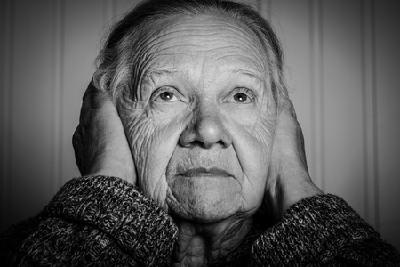 Portrait of an elderly woman with hands near face on a light background. Toned.の写真素材
