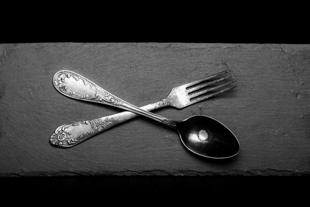 Fork and spoon on a plate of slate on a black background. Toned.の写真素材
