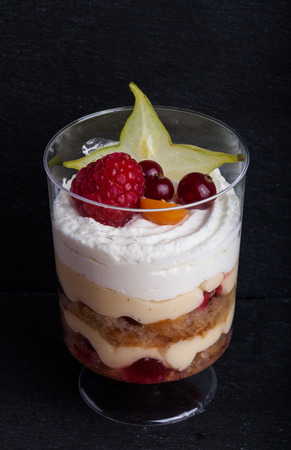 Small snacks trifle with fruits and cream in plastic glass on a black slate plate.の写真素材
