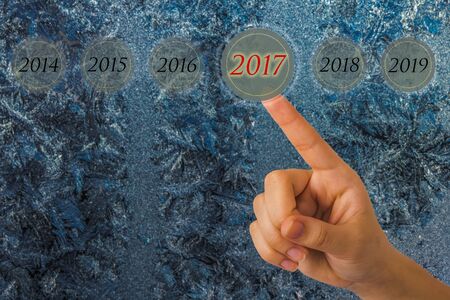 Hand of a young girl points to a figures 2017 opposite beautiful nature pattern on frosted glass for...