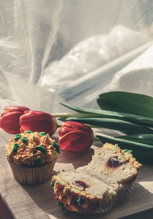 Yummy cupcake and red tulips on light background. Selective focus. Toned.