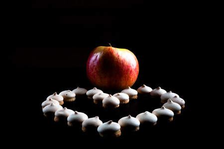 Small cookies laid in the shape of heart and ripe apple on black background. Selective focus. Shallow depth of field. Toned.の写真素材