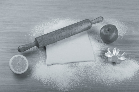 Set for home baking on a light wooden table with flour. Rolling pin, baking form, dough, half of lemon, apple. Toned.の写真素材