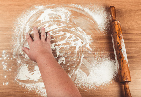 Plump women's hands work with dough on a light wooden table. Toned.の写真素材