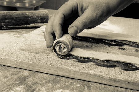 Female hand sprinkles apple slices on the dough strip on a light wooden table with flour. Toned.の写真素材