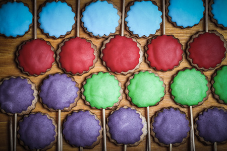 Gingerbread cookies with colored mastic on sticks on the old wooden cutting board. Toned.の写真素材