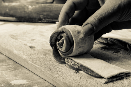 Female hand sprinkles apple slices on the dough strip on a light wooden table with flour. Selective...