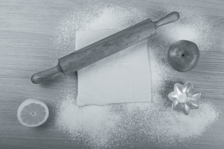 Set for home baking on a light wooden table with flour. Rolling pin, baking form, dough, half of lemon, apple. Toned.の写真素材