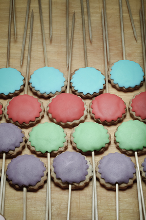 Gingerbread cookies with colored mastic on sticks on the old wooden cutting board. Toned.の写真素材