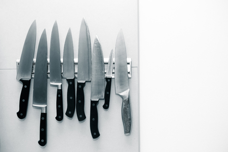 Kitchen knives set on a magnet on a light wall for background. Toned.の写真素材