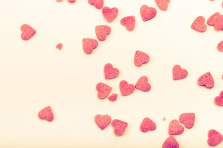 Many pink sugar hearts are scattered on a light background. Toned.