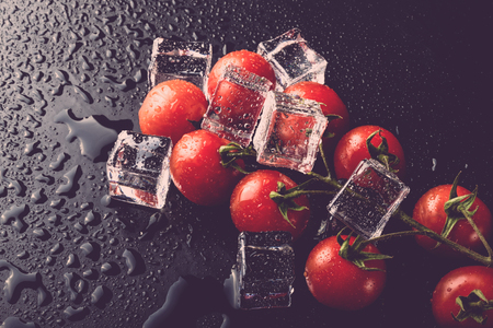 Banch of red cherry tomatos and ice cubes on black wet table. Selective focus. Toned.の写真素材